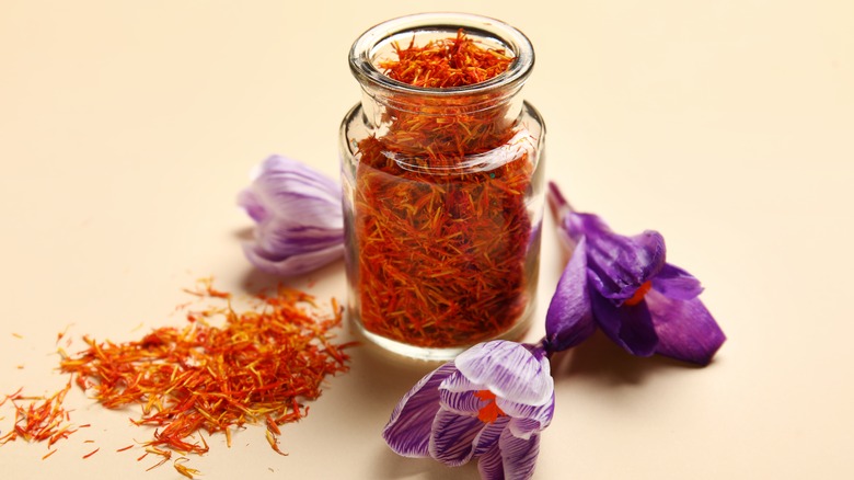 Jar of saffron next to three crocus flowers and spread out saffron strands