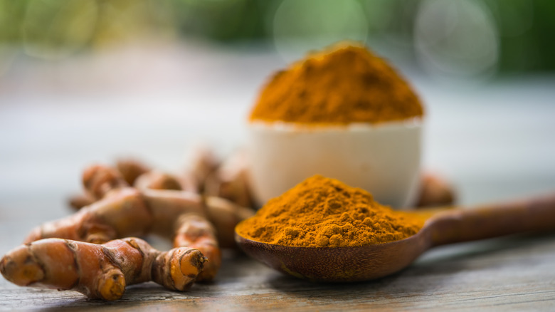 spoonful of turmeric next to fresh turmeric and full bowl