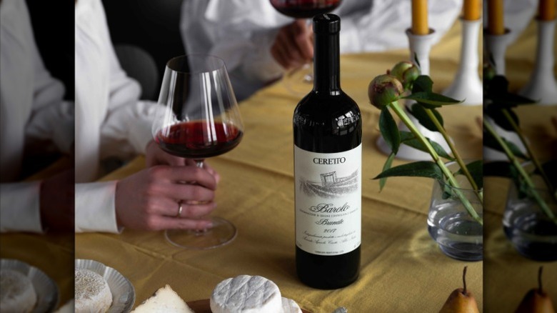 Person holding a glass of Ceretto Barolo DOCG Brunate alongside bottle and cheese