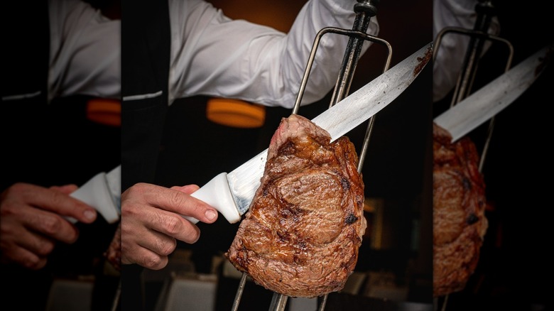 Waiter carving steak on skewer