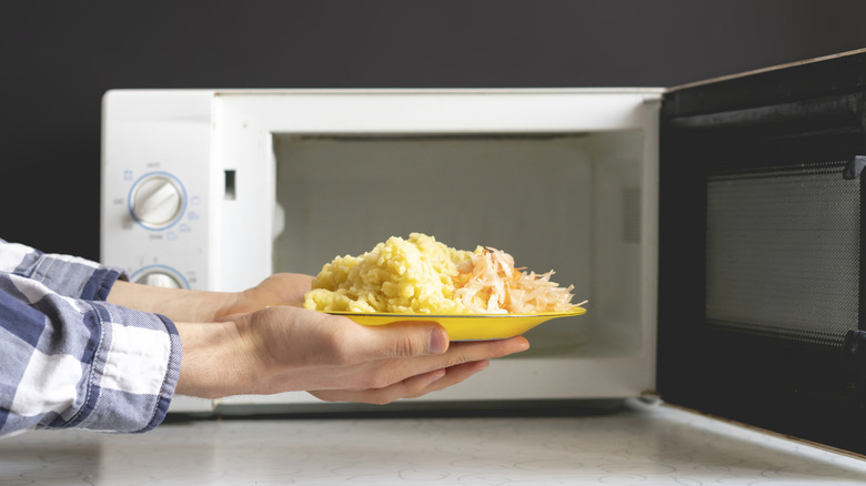 Hands holding plate of food in front of open microwave