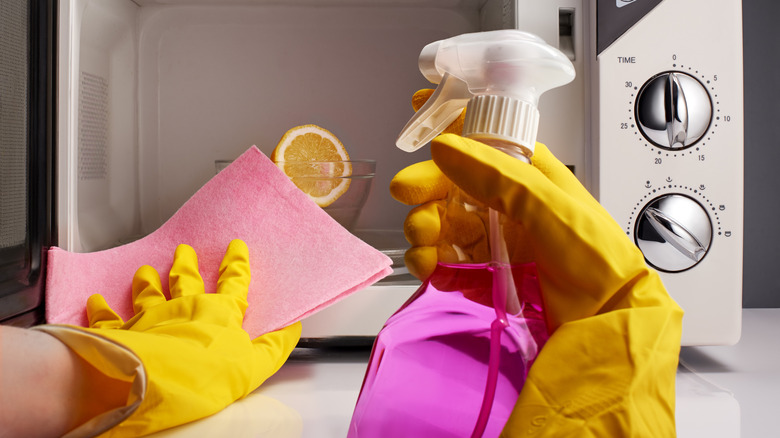 Gloved hands cleaning microwave with spray bottle and cloth