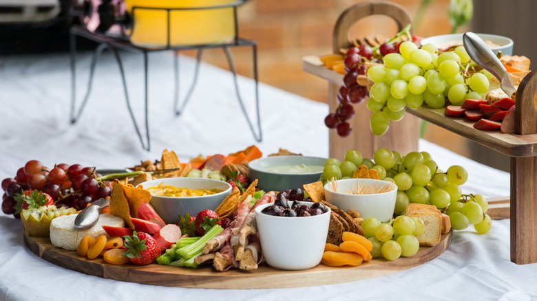 wooden charcuterie board loaded with meats, fruits, nuts, cheese, and crackers on grazing table