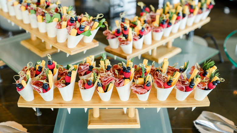 Charcuterie cups with cheese, meat, and toppings in a display stand