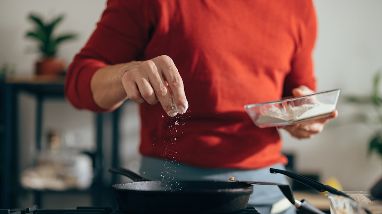 Person salting skillet on stove