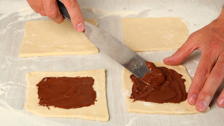 Man spreading chocolate on puff pastry while leaving a border