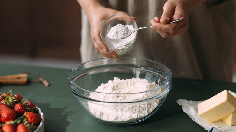 Woman putting baking powder into flour