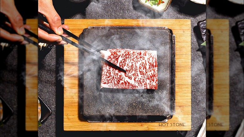 beef cooking on stone with chopsticks