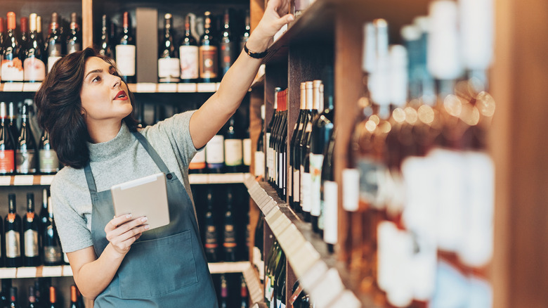 Wine shop owner holding a digital tablet and arranging bottles