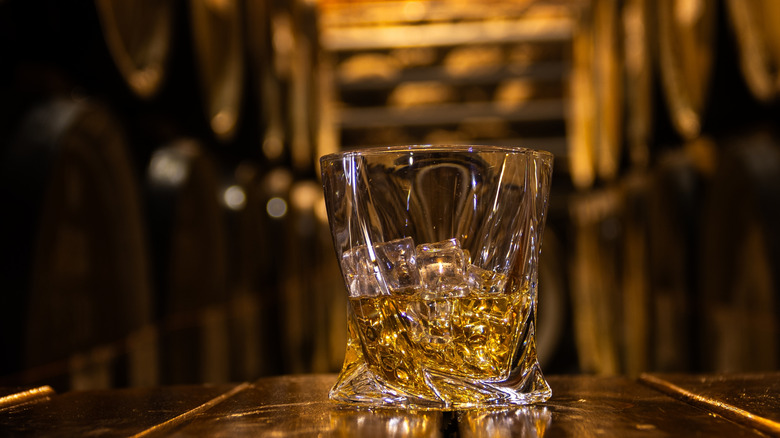 Glass of whiskey with ice on an old wooden barrel
