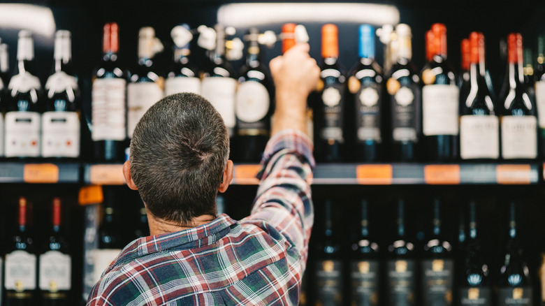 Man reaching for a bottle of wine while shopping in the aisle of a liquor store