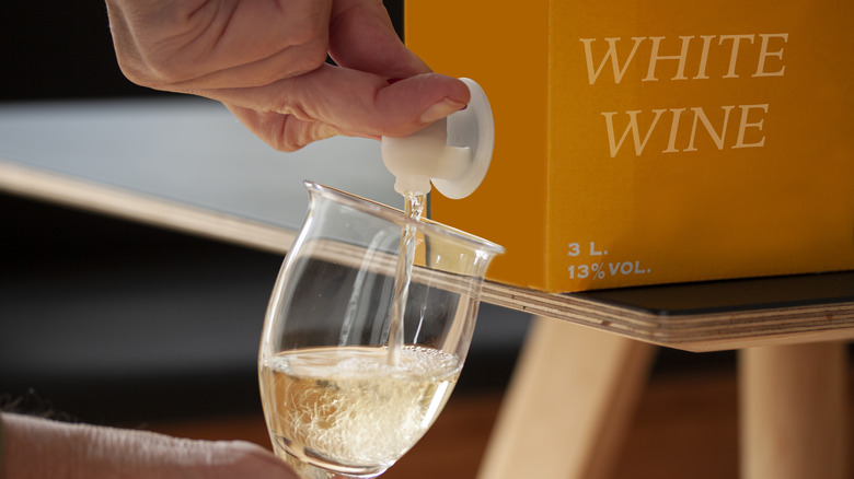 Hand pouring white wine into a glass from a box