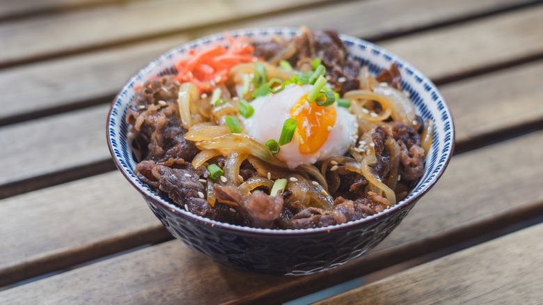 A gyudon beef bowl topped with scallions and a soft egg