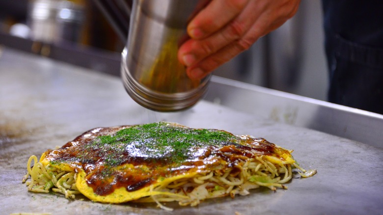 Hand seasoning an okonomiyaki or Japanese savory pancake