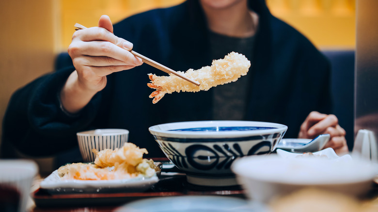 Hand holding a shrimp tempura with chopsticks in a restaurant