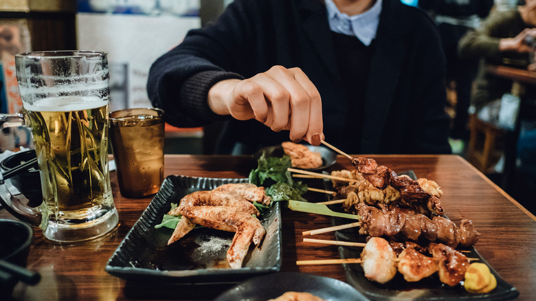 Woman enjoying a beer and a chicken yakitori skewer in a restaurant