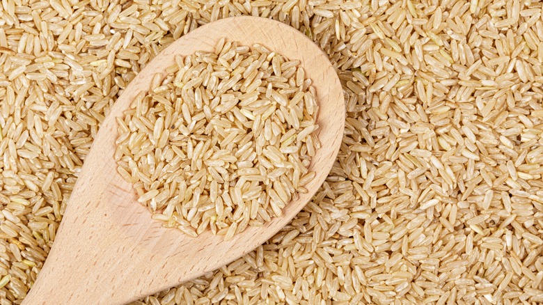 Pile of uncooked brown rice grains with wooden spoon