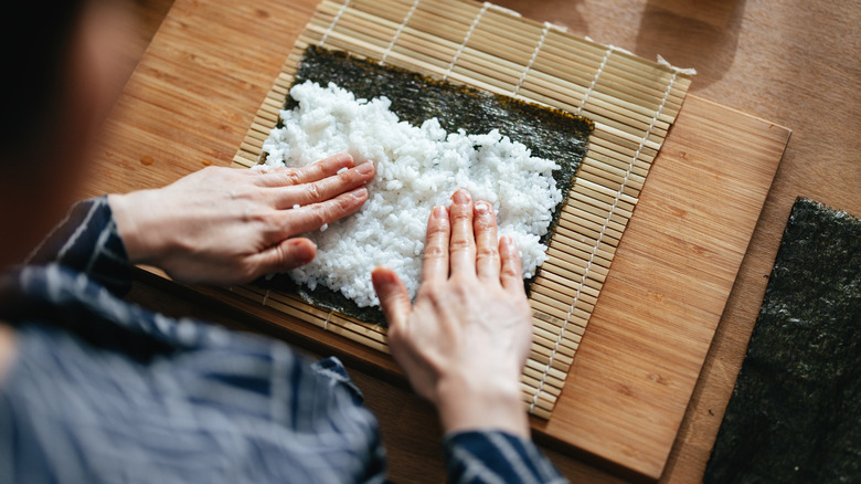 Woman pressing cooked sushi rice onto a sheet of nori