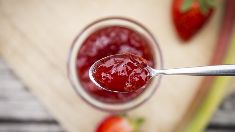 Spoon of red strawberry jam over jar