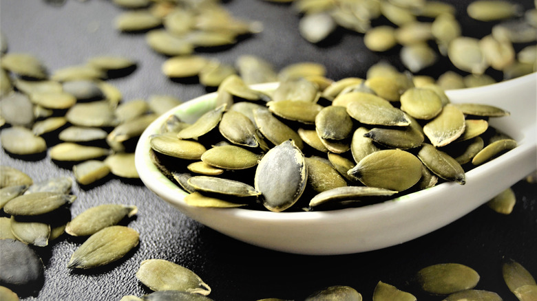 Pumpkin seeds on white spoon on black table