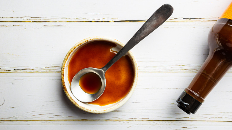 Worcestershire sauce in bowl on wooden table with silver spoon