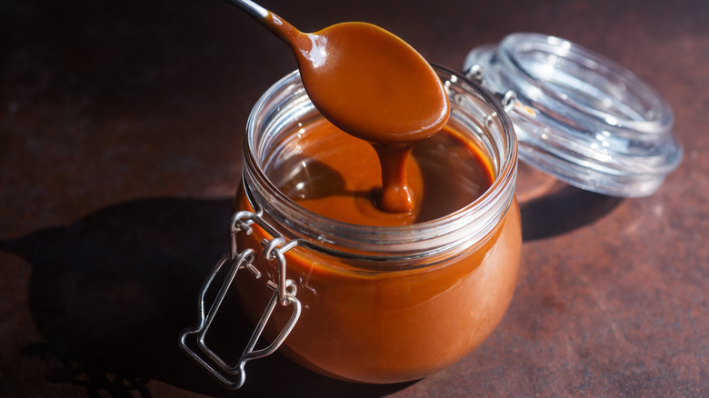 Spoon in caramel sauce on brown surface