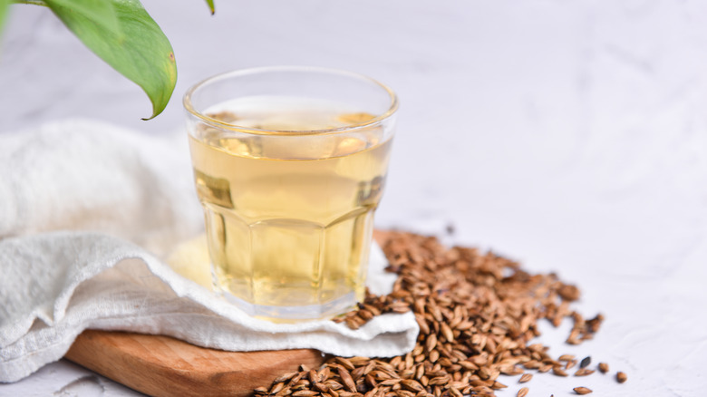 Cup of barley tea on wooden board, white fabric, and pile of barley