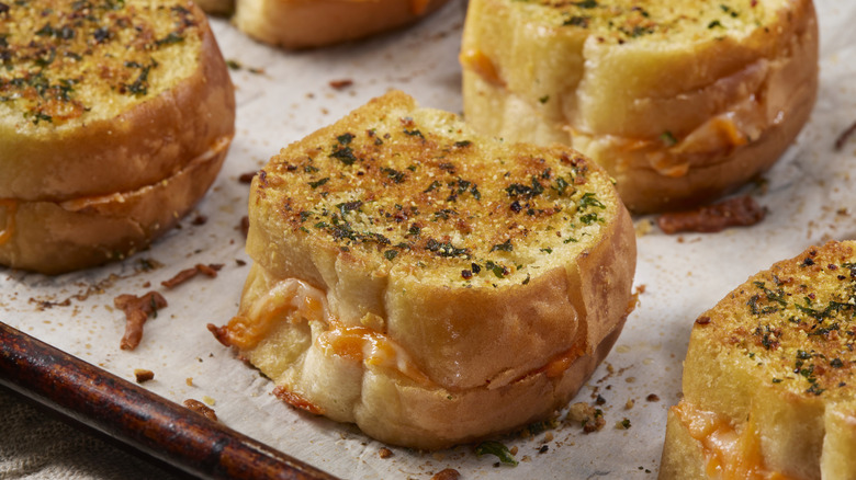 Tiny cheese sadnwiches sprinkled with herbs on baking sheet
