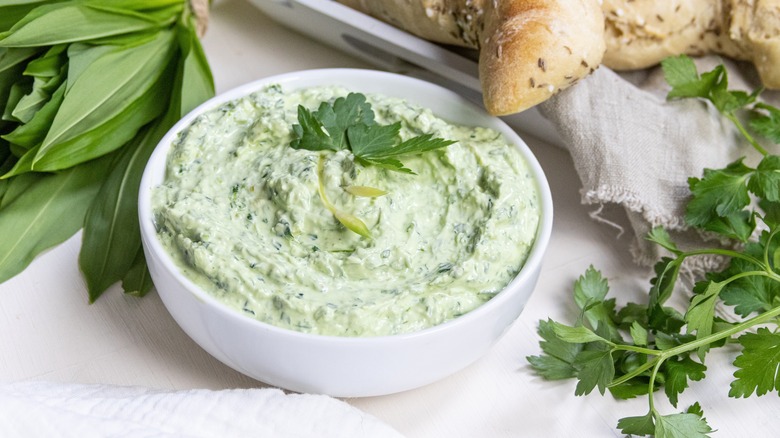 yogurt with fresh herbs in white bowl near bread