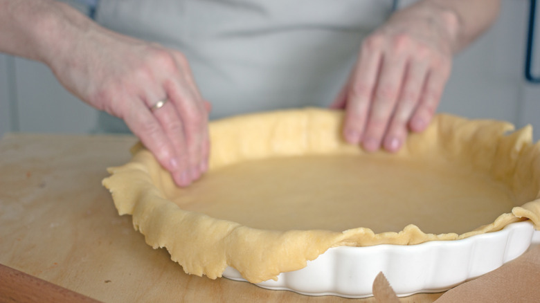 Hands pressing dough into dish