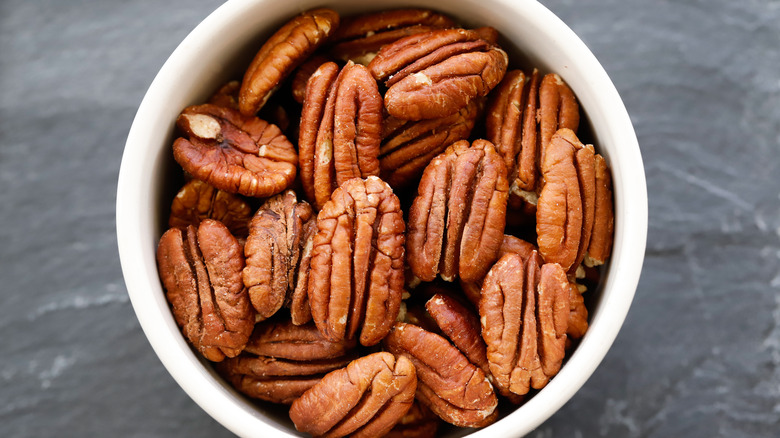 Top view, close-up of fresh, plump pecans in a white bowl with a gray background