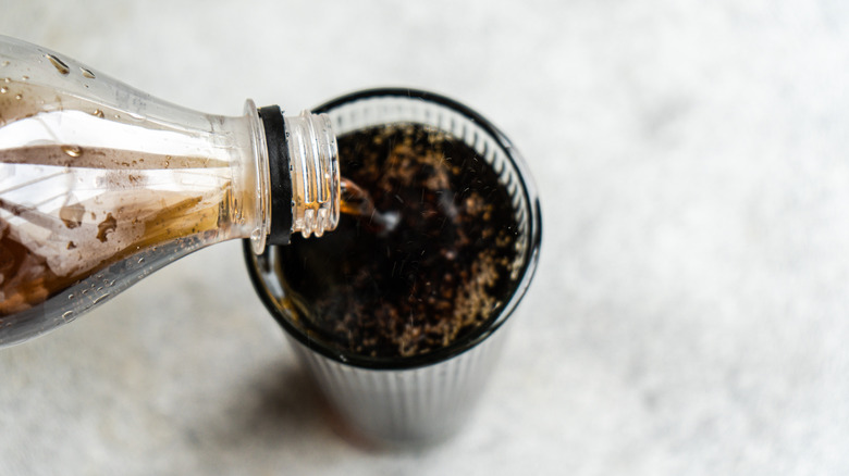 Pouring Coca-Cola from a plastic bottle into a glass set on a light background