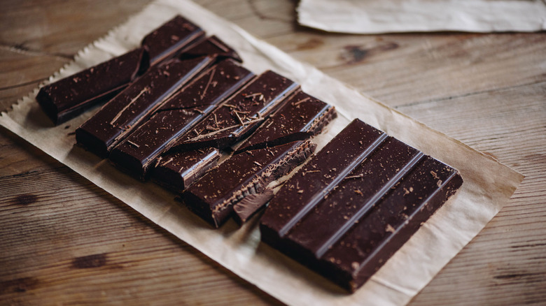 Broken dark chocolate bar spread on a brown paper bag on a wood background