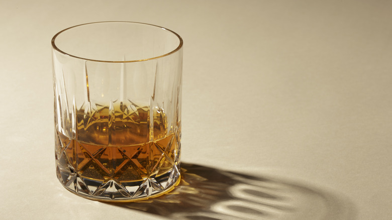 Crystal glass filled half-way with brown bourbon on a light brown background