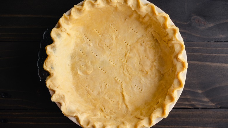 Unbaked, homemade pie crust pressed into a pan with decorative edges and pierced bottom on a dark brown background