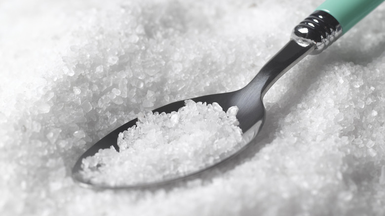 Close-up of a metal spoon surrounded by salt, holding some salt crystals