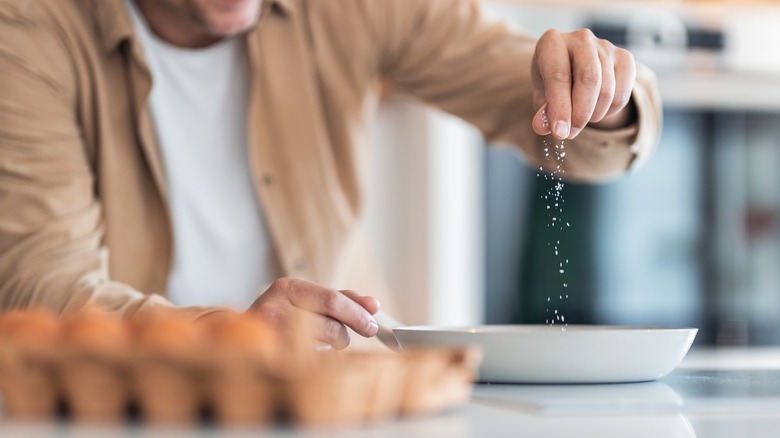 person adding salt to eggs