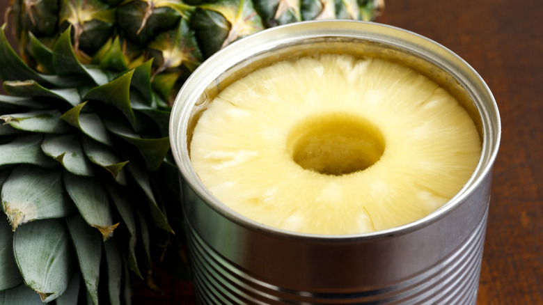 Pineapple rings in tin on dark wood next to pineapple