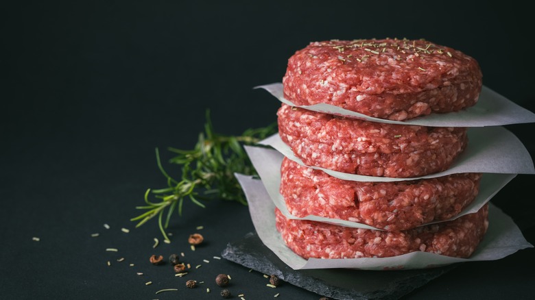 Stack of raw burger patties with herbs