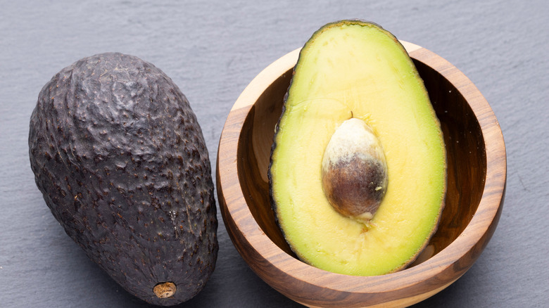 whole avocado next to half of an avocado in bowl