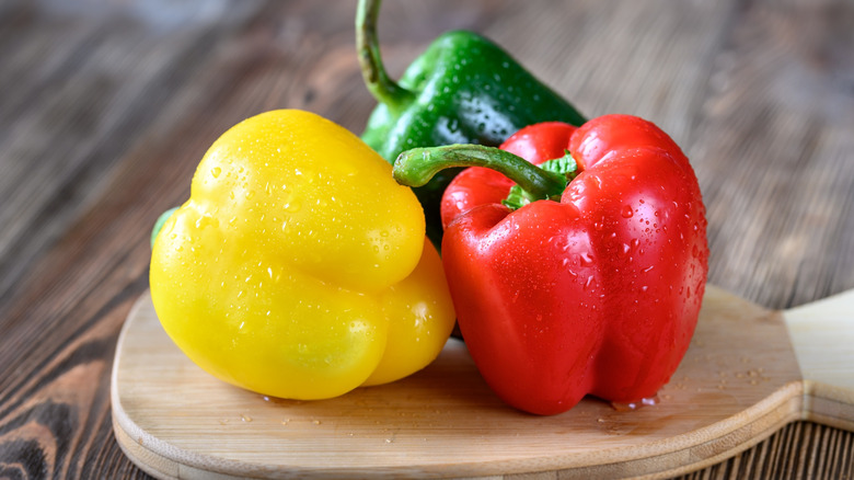 yellow, red, and green peppers with water droplets on wooden surface