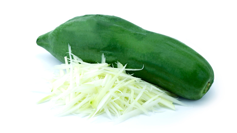 green papaya whole and chopped against white background