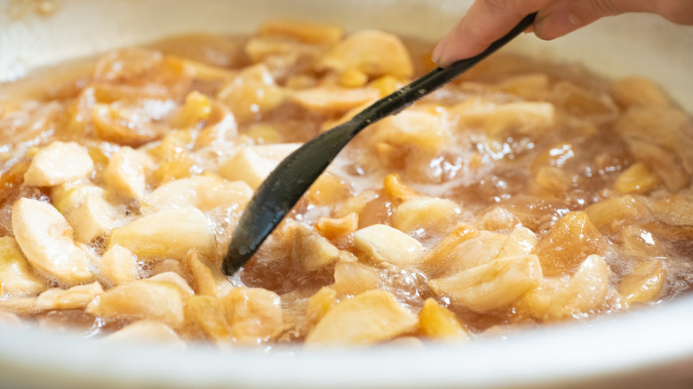 Cooking down sliced apples on stovetop with spoon