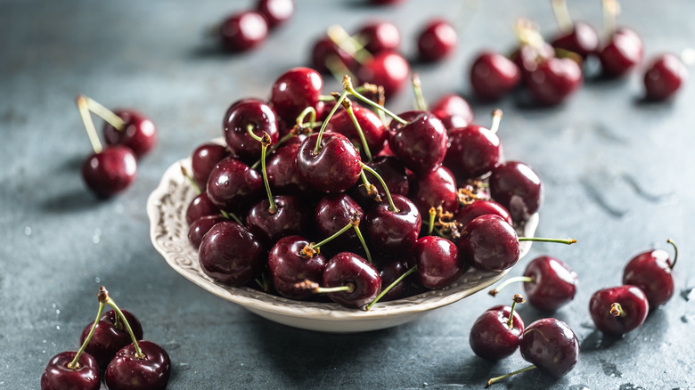 Pile of cherries on dish with cherries surrounding the dish