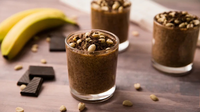 Cups of rich chocolate peanut butter chia pudding with banana and nuts on the side