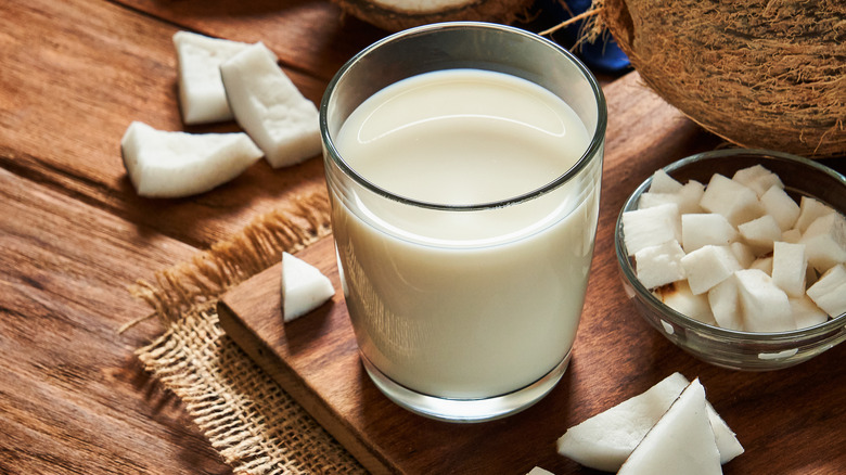 Glass of non-dairy coconut milk on rustic wooden table with coconut pieces