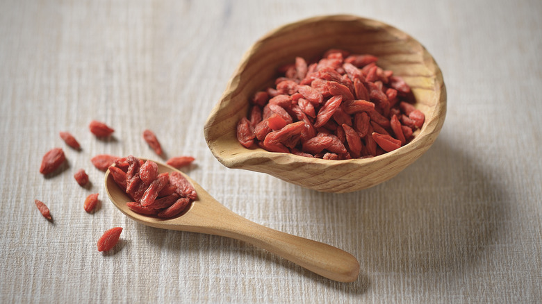 goji berries in a wooden bowl and wooden spoon holding goji berries on the side