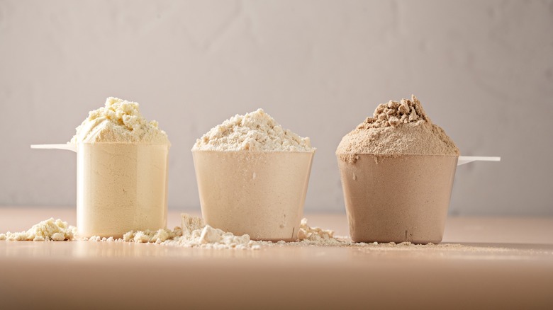 Three measuring cups filled with big heaps of different colored whey protein powder