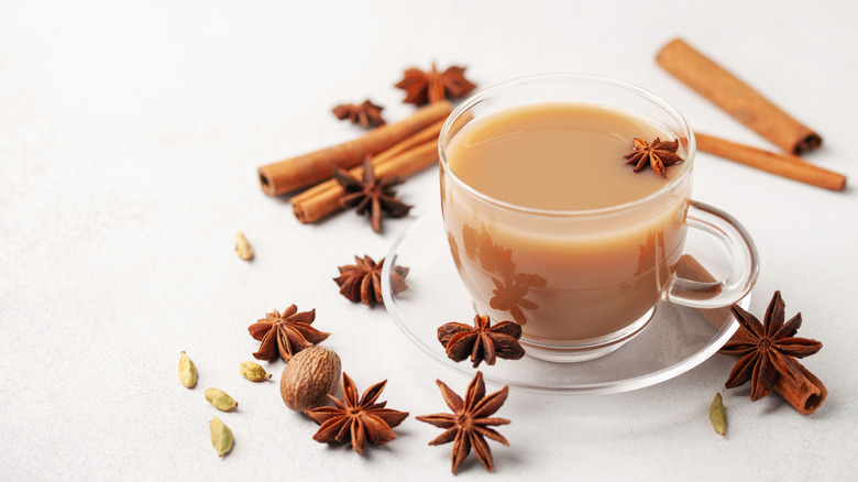 Whole chai spices surrounding a glass mug of tea