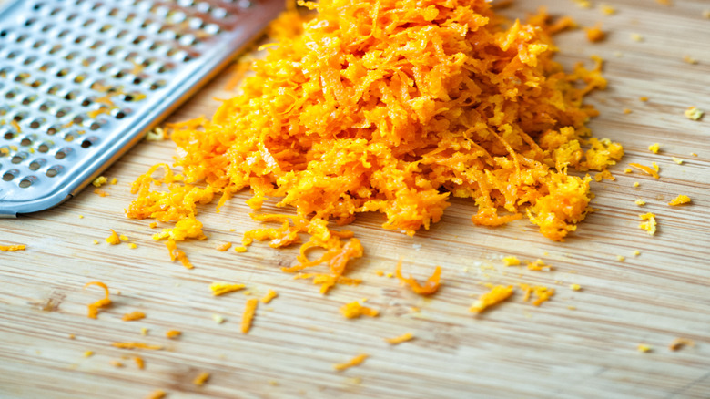 Pile of orange zest next to a grater and oranges